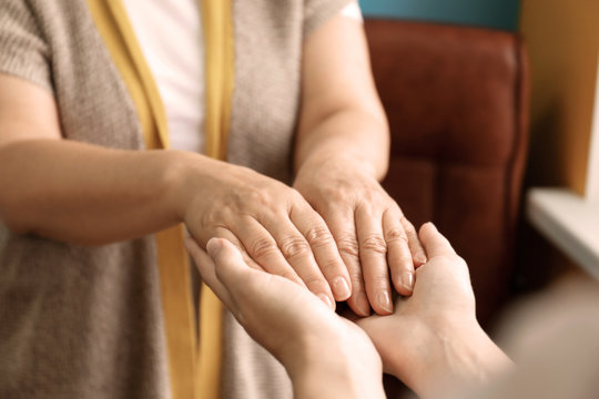 Young woman holding hands of her mother, closeup. Concept of care and support