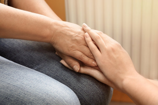 Young woman holding hands of her mother, closeup. Concept of care and support