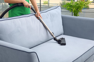 Woman cleaning couch with vacuum cleaner at home