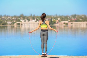 Fototapeta na wymiar Young woman skipping rope near river