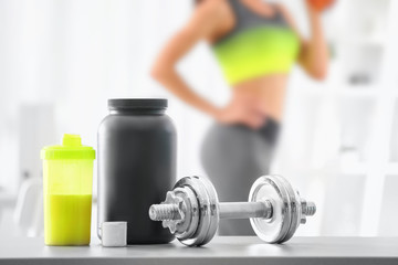 Fototapeta na wymiar Composition with metal dumbbell, protein shake and blurred woman on background