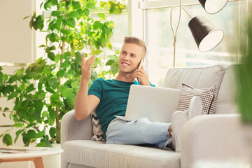 Young man with laptop and cell phone on sofa at home