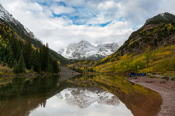 Fototapeta na wymiar Maroon Peak and its reflection on Maroon Lake and aspen trees with its gold yellow leaves in fall foliage autumn season in a bright day light sunny day cloudy blue sky, Aspen, Colorado, USA.