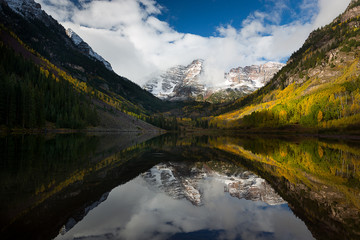 Plakat Maroon Peak and its reflection on Maroon Lake and aspen trees with its gold yellow leaves in fall foliage autumn season in a bright day light sunny day cloudy blue sky, Aspen, Colorado, USA.