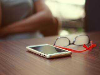 A woman is waiting for an appointment in a coffee shop by placing a mobile phone and red glasses on the table in front of her.