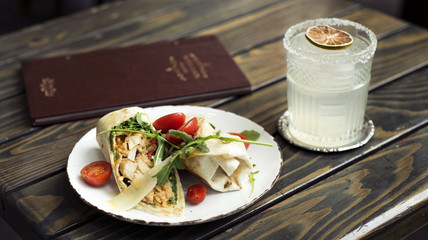 chicken wrap with tomatoes and wild rocket on top with cocktail on wooden table