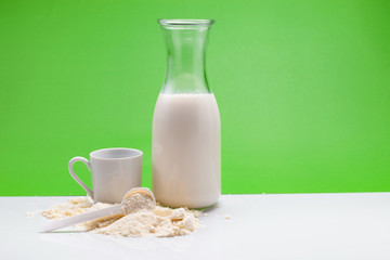 Bottle of fresh milk with powdered milk and spoon for baby on white table,green background.