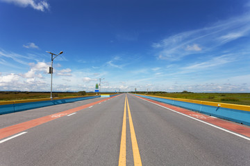 Asphalt road with green grass field countryside scenery blue sky white cloud background.