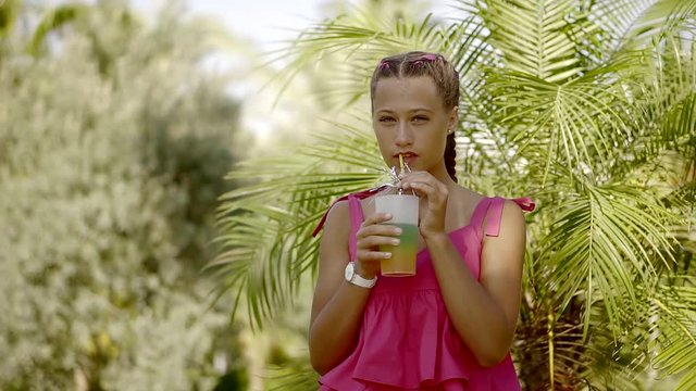 A young girl drinks a soft drink from a plastic glass with a straw, she put juice to her lips