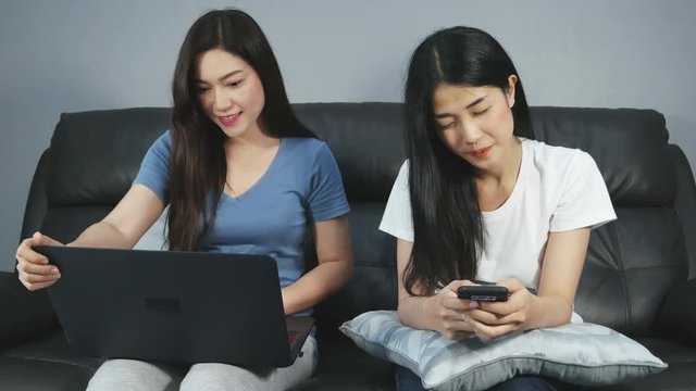 4k of two Asian women are using a smartphone  and working on laptop computer in living room