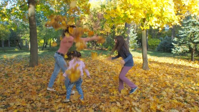 Happy family playing with leaves in autumn park. Mother and daughter throw yellow leaves.