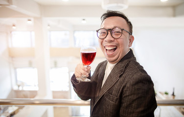 Happy Asian rich man smiling while holding a glass of red wine in the party hall
