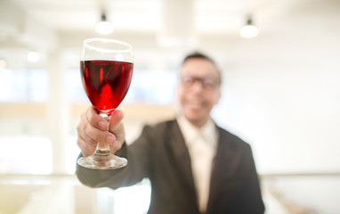 Happy Asian rich man smiling while holding a glass of red wine in the party hall