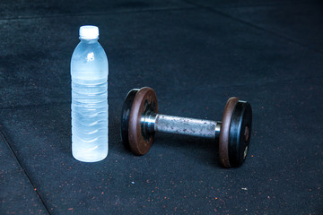 Obraz na płótnie Canvas Cool drinking water with dumbbell on floor in fitness gym. Selective focus.