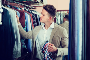 Fototapeta na wymiar young guy deciding on new shirt in men’s cloths store