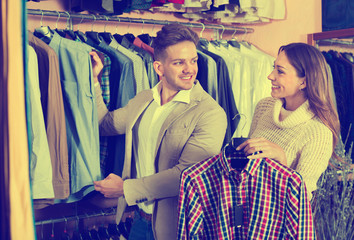 Fototapeta na wymiar Couple deciding on new shirt in men’s cloths store