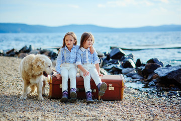 Two little twin sisters on a walk with dog on the beach.