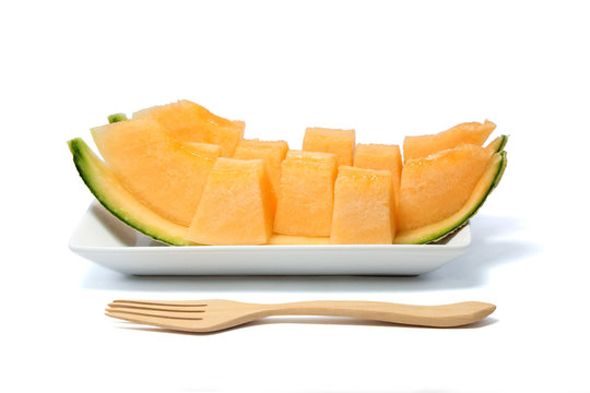 Sliced melon in pieces arranged on white dish with wooden fork isolated on white background.