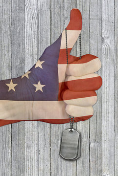 American flag hand with thumbs up hand gesture and military dog tags on gray weathered wood