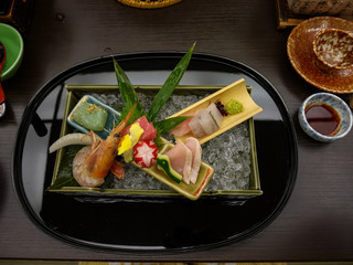 Japanese ryokan kaiseki dinner decorative sashimi set including Pacific blue fin tuna, shrimp, greater amberjack, halfbeak, konjac in ooishi on crushed ice tray with wasabi and soy sauce