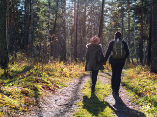 Fototapeta premium Young couple in love holding hands and walking through a park on a sunny autumn day. Casual style of clothes and accessories.