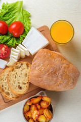 Breakfast from bread, cheese, tomatoes, potatoes and all-over salad on a wooden table closeup.
