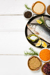 Healthy food diet river fresh raw fish omega 3 on pan with olive oil spoon of sea salt peppercorns grains lentils quinoa beans peas rosemary leaves on white wooden table background top view copy space
