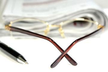 Eye glasses, pen and newspaper on the table.