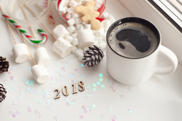 Cup of coffee with Christmas sweetness on white table close-up, number of year 2018