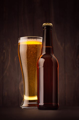 Brown beer bottle and glass weizen with golden lager on dark wood board, vertical, mock up. Template for advertising, design, branding identity.