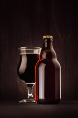 Brown beer bottle and glass tulip with porter on dark wood board, vertical, mock up. Template for advertising, design, branding identity.