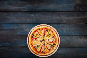 Delicious pizza with mushrooms chicken sweet peppers and olives on a dark wooden background. Top view bottom orientation