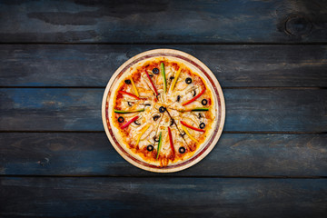 Delicious pizza with mushrooms chicken sweet peppers and olives on a dark wooden background. Top view center orientation
