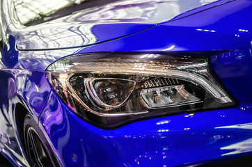 The headlamp of a blue sports car of aggressive form with a part of the hood and black wheel, bumper and partronik