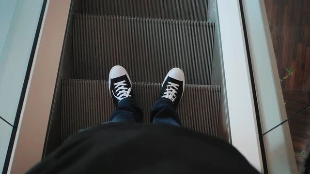Closeup top view on man legs in sneakers traveler using moving escalator in business center or shopping mall. Slow motion