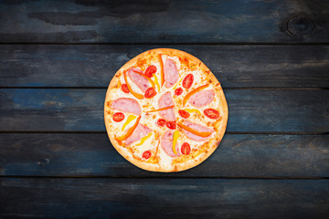 Delicious pizza with ham sweet peppers and tomatoes on a dark wooden background. Top view center orientation