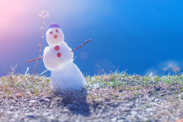 Llittle snowman in a blue cap on the grass in the sunlight