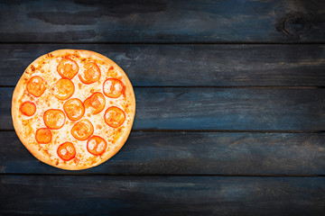 Perfect pizza margarita with tomato slices on a dark wooden background. Top view orientation on the left side