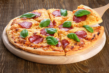 Pepperoni pizza with salami and basil on dark wooden background.