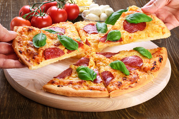 Pepperoni pizza with salami and basil on dark wooden background.