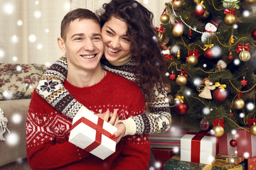 Happy couple give gifts in christmas decoration at home. New year eve, ornated fir tree. Winter holiday and love concept.