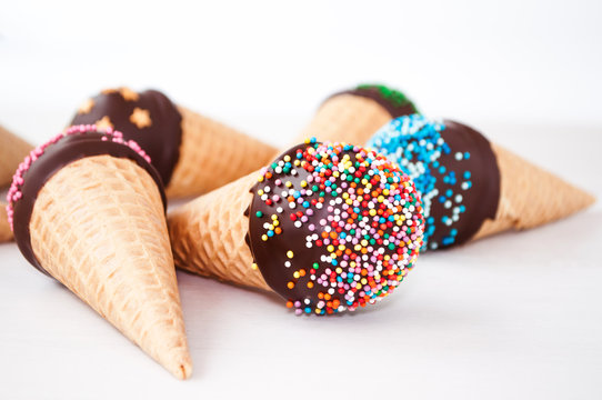 Chocolate Cake Pops In Waffle Cone For Ice Cream In Assortment, Decorated With Confectionery Sprinkles On White Wood Table. Picture For A Menu Or A Confectionery Catalog.