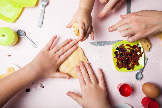 Mom teaches young children how to cook. Hands knead the dough, children's utensils.