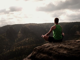 Naklejka na ściany i meble Man on top of mountain in yoga pose. Exercise yoga on edge with a breathtaking view