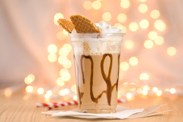 Close-up of delicious refreshing drink decorated with whipped cream and cookies on background of magic garland.