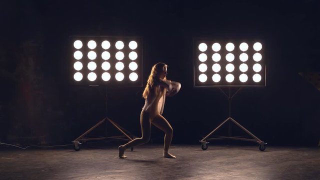 a young woman of pleasant appearance dances in the training hall in the lighting of searchlights in the background. the girl professional dance performs the set number in the style of classical and