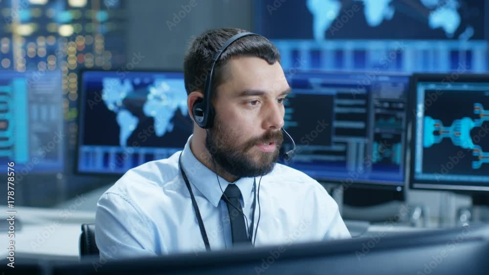 Poster System Control Room Dispatcher Talks into Headset. He Controls Correct Work of the Facility. In the Background Multiple Monitors Show Technical Data. Shot on RED EPIC-W 8K Helium Cinema Camera.