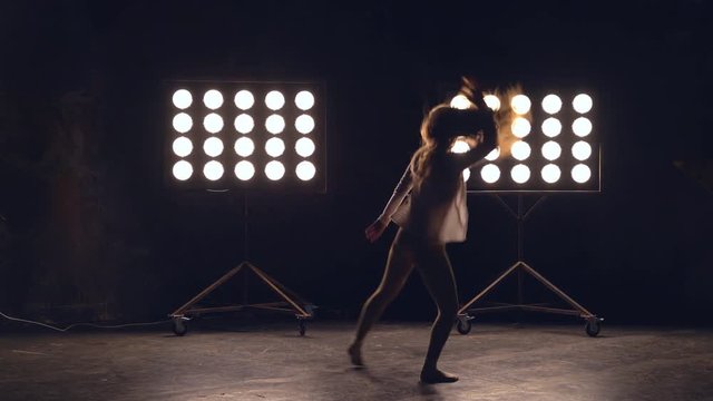 a young woman of pleasant appearance dances in the training hall in the lighting of searchlights in the background. the girl professional dance performs the set number in the style of classical and