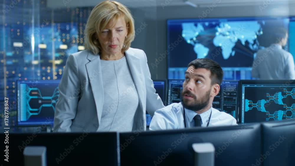 Poster In the System Monitoring Room Senior Technical Supervisor Controls Work of the Operator. In the Background People Working and Monitors Showing Relevant Technical Data. 