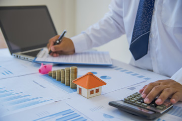 Closeup of new homeowner signing a contract of house sale or mortgage papers with a wooden toy house on the document. Suitable for real estate concept.